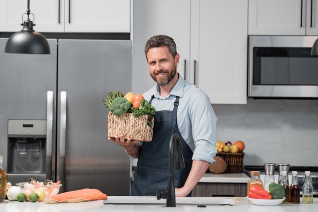 Homme en tablier de cuisinier avec des légumes en prenant soin de la santé bel homme en tablier de chef cuisiner des légumes