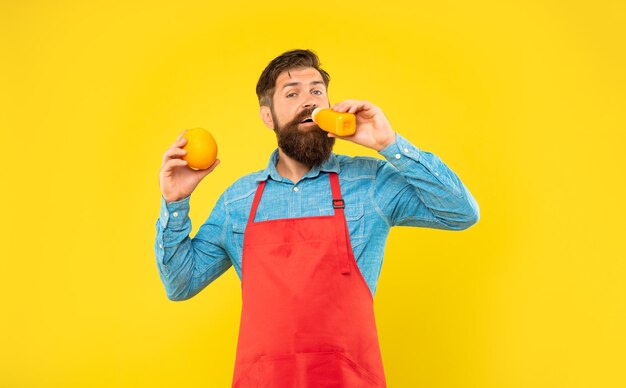 Homme en tablier faire semblant de boire du jus d'orange fond jaune barman de jus