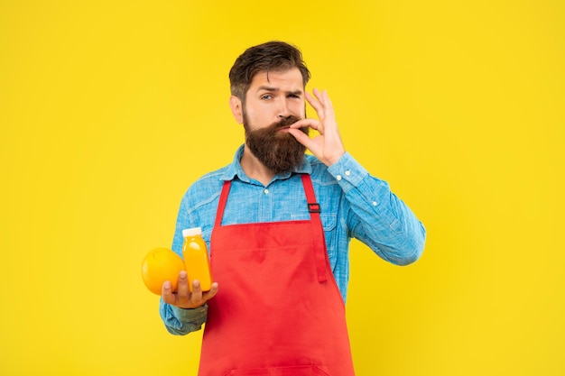 Homme en tablier léchant le doigt tenant une bouteille de jus d'orange et de jus fond jaune barman de jus