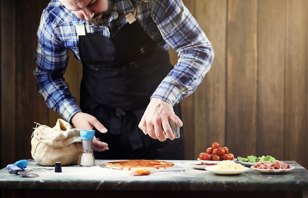 Homme en tablier préparant une pizza, pétrir la pâte et mettre les ingrédients