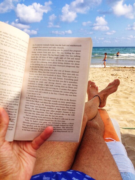 Photo un homme taillé lisant un livre se détendant sur la plage contre le ciel