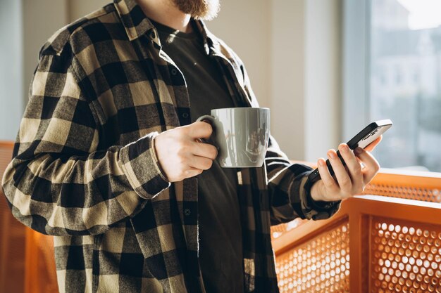 Un homme avec une tasse de café et un smartphone le matin au bureau