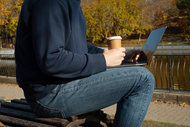 Homme avec une tasse en papier et un ordinateur portable dans le parc