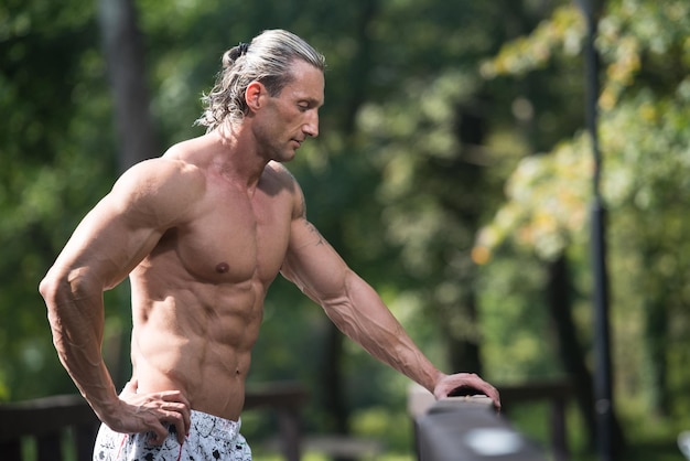 Homme de tatouage mature en bonne santé debout fort à l'extérieur dans la nature et muscles de flexion Modèle de forme physique de bodybuilder athlétique musclé posant après des exercices