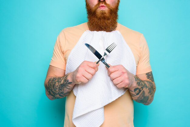 L'homme avec des tatouages est prêt à manger avec des couverts à disposition