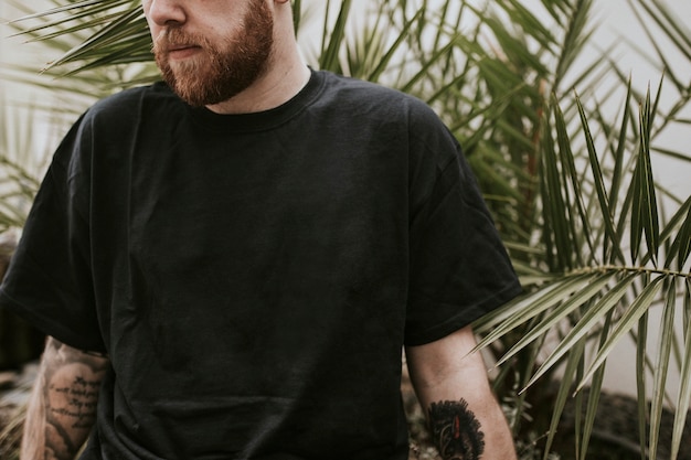 Homme tatoué debout près des feuilles de palmier