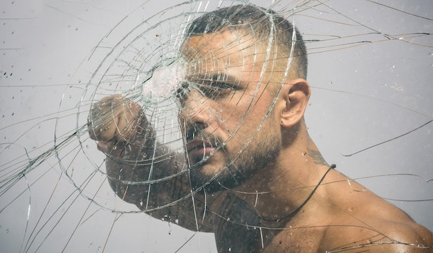 Homme tatoué hispanique sexy derrière du verre brisé Trou de balle dans le verre Concept de test de destruction et d'écrasement Style homme Macho homme verrier derrière du verre pilé