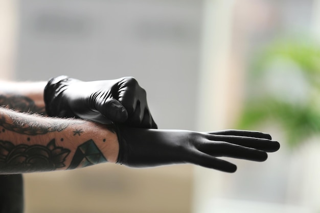 Homme tatoué portant des gants en latex noir sur fond flou