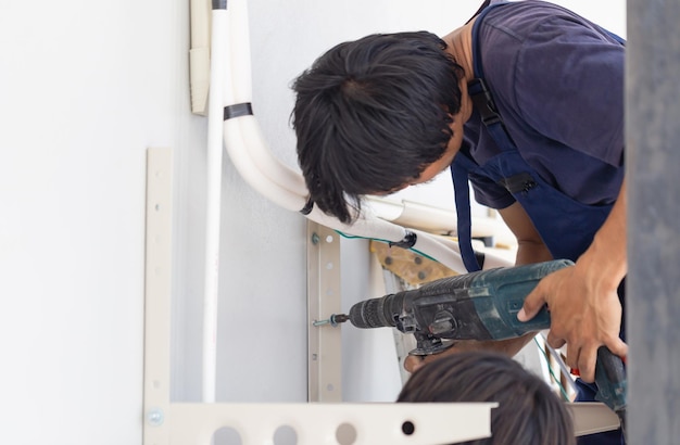 Homme technicien avec marteau perforateur installant une climatisation dans une maison de client Jeune réparateur réparant l'unité de climatisation Concepts d'entretien et de réparation