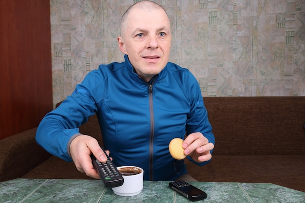 L'homme avec la télécommande de la télévision à la main, buvant du café et regardant une émission de télévision