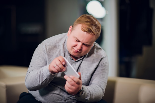 Homme avec téléphone surpris en jouant à des jeux assis sur le canapé au bureau