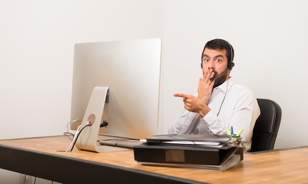 Homme télévendeur dans un bureau, pointant le doigt sur le côté avec un visage surpris