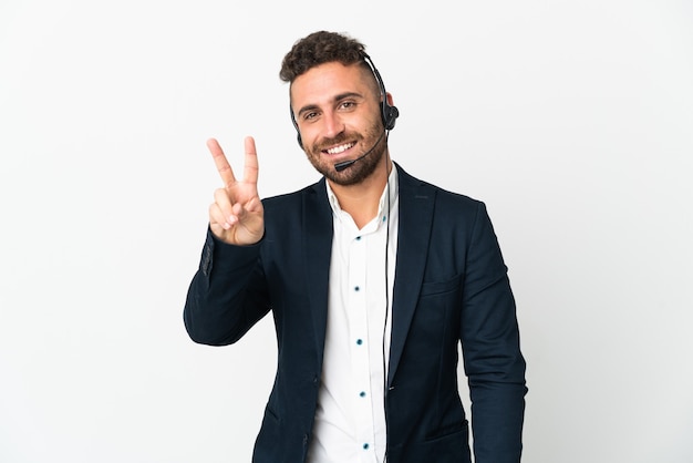 Homme de télévendeur travaillant avec un casque isolé sur blanc souriant et montrant le signe de la victoire