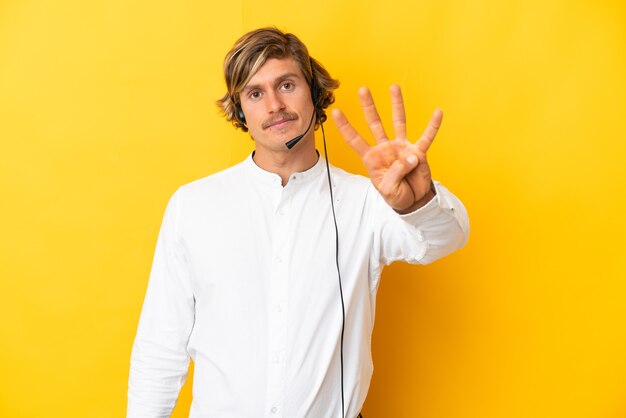 Homme de télévendeur travaillant avec un casque isolé sur jaune heureux et en comptant quatre avec les doigts