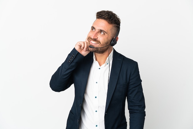 Homme de télévendeur travaillant avec un casque isolé sur un mur blanc en pensant tout en levant