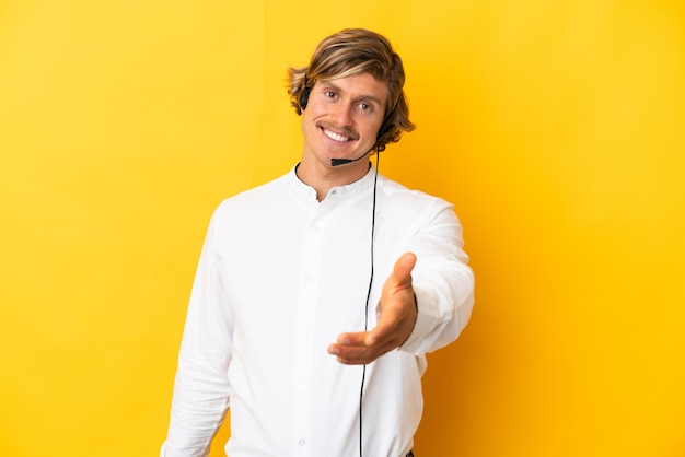 Homme de télévendeur travaillant avec un casque isolé sur un mur jaune se serrant la main pour conclure une bonne affaire