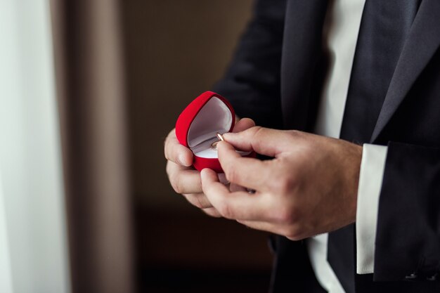 Photo homme tenant des anneaux de mariage se trouvent dans une belle boîte, le marié se prépare le matin avant la cérémonie