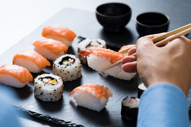 Homme tenant des baguettes et manger des sushis au restaurant