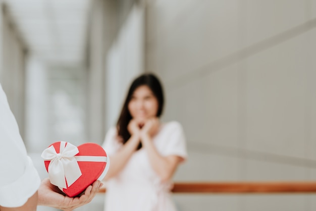 Homme tenant une boîte cadeau en forme de coeur rouge présente pour surprendre une femme