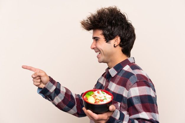 Homme tenant un bol plein de nouilles pointant vers le côté pour présenter un produit