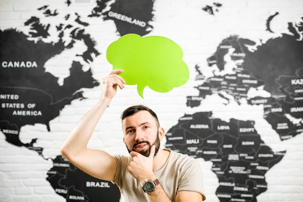 Homme tenant une bulle colorée au-dessus de la tête assis au bureau avec une carte du monde en arrière-plan rêvant de voyager