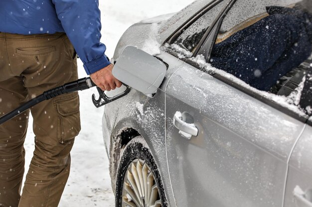 Homme tenant une buse de carburant, remplissant le réservoir d'essence d'une voiture recouverte de neige en hiver