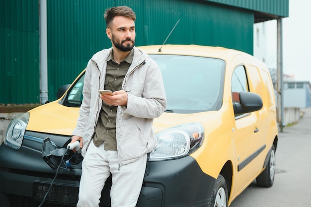 Homme tenant un câble de charge pour voiture électrique dans un parking extérieur Et il va connecter la voiture à la station de charge dans le parking près du centre commercial