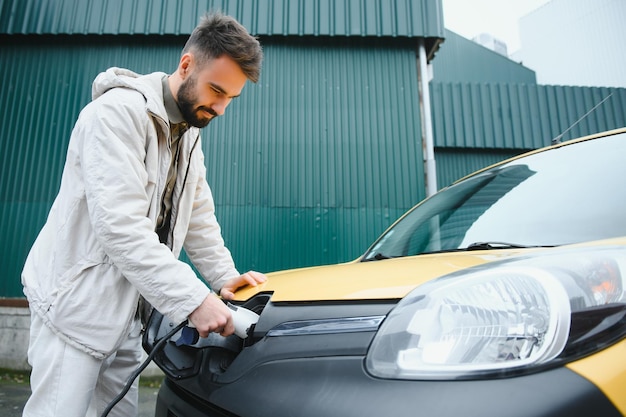 Homme tenant un câble de charge pour voiture électrique dans un parking extérieur Et il va connecter la voiture à la station de charge dans le parking près du centre commercial