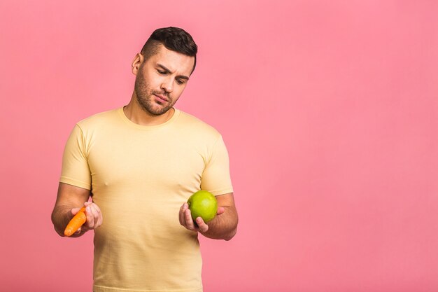 Homme tenant la carotte et la pomme. Végétarien préparant un repas. Un mec souriant aime les fruits et légumes.