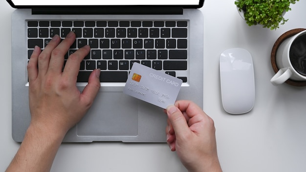 Homme tenant une carte de crédit et utilisant un ordinateur portable pour effectuer un paiement en ligne.