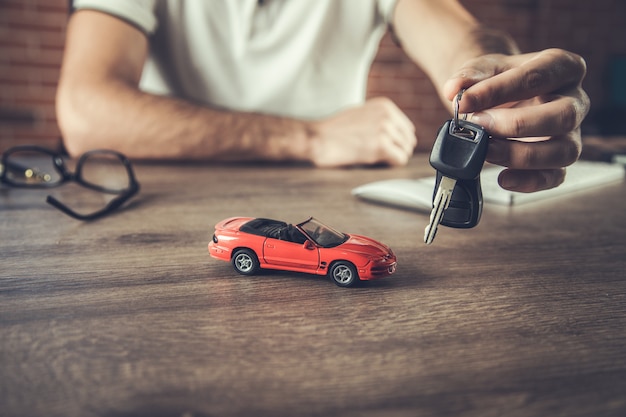 Homme tenant la clé avec le modèle de voiture sur la table