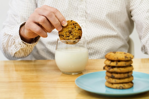 Homme tenant un cookie aux pépites de chocolat sur un verre de lait et sur une table en bois