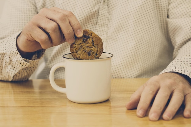 Homme tenant un cookie sur une tasse de lait blanc sur un fond en bois