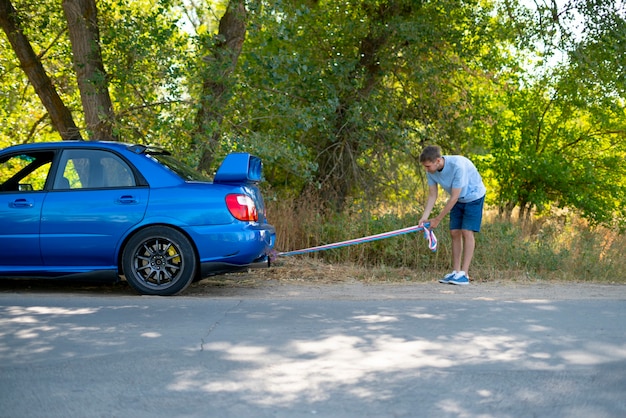 L'homme tenant une corde de remorquage et l'installer sur le crochet de la voiture, l'accident de voiture et le problème avec le moteur