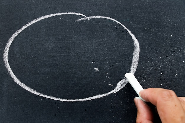 Homme tenant une craie blanche pour écrire quelque chose sur un tableau noir avec fond de cercle