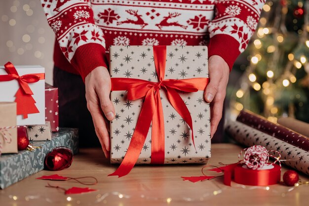 Homme tenant dans les mains une boîte-cadeau enveloppée dans du papier kraft et un ruban rouge sur fond d'arbre de Noël