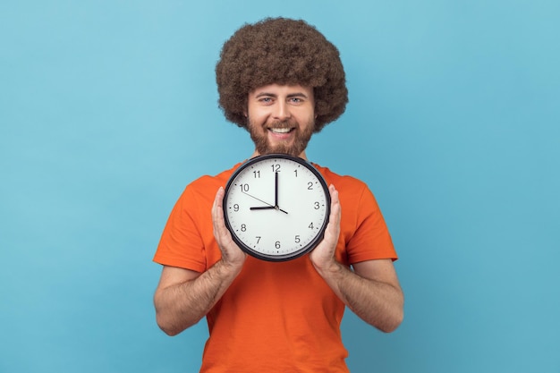 Homme tenant dans les mains une grande horloge murale regardant la caméra avec une expression heureuse