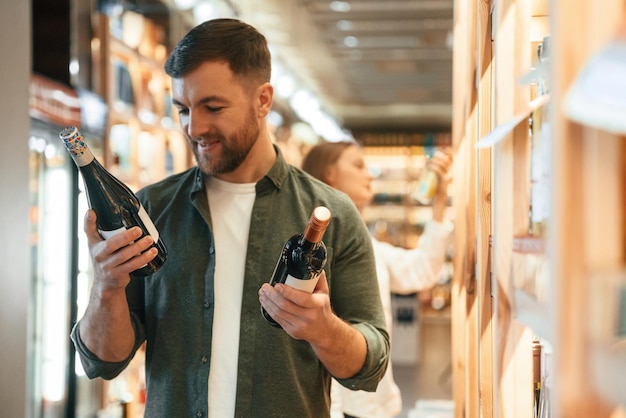 Un homme tenant deux bouteilles dans les mains Un homme et une femme choisissent du vin dans le magasin