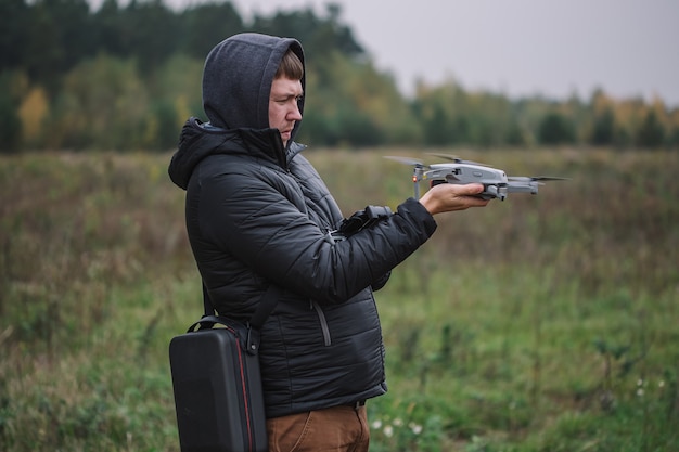 Homme tenant un drone et une télécommande sur fond de terrain.