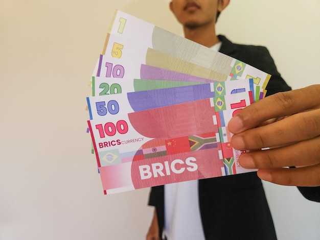 Homme tenant une illustration de la monnaie BRICS qui pourrait ébranler la domination du dollar
