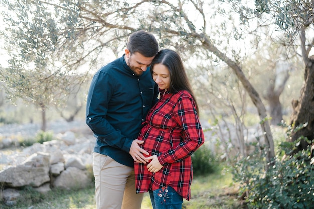 Homme tenant la main sur le ventre d'une femme enceinte en se tenant près d'un arbre