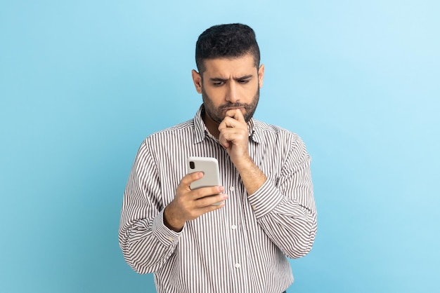 Homme tenant le menton avec un smartphone à la main envisageant de mettre à jour le logiciel en choisissant les tarifs