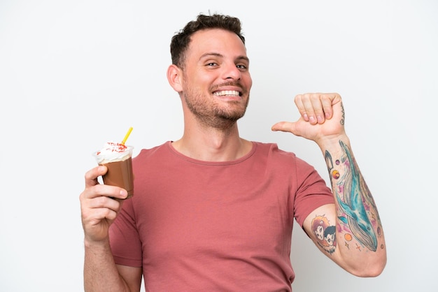 Un homme tenant un milk-shake au chocolat avec un pouce pointant vers la gauche.