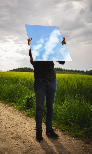 Photo un homme tenant un miroir avec le reflet des nuages