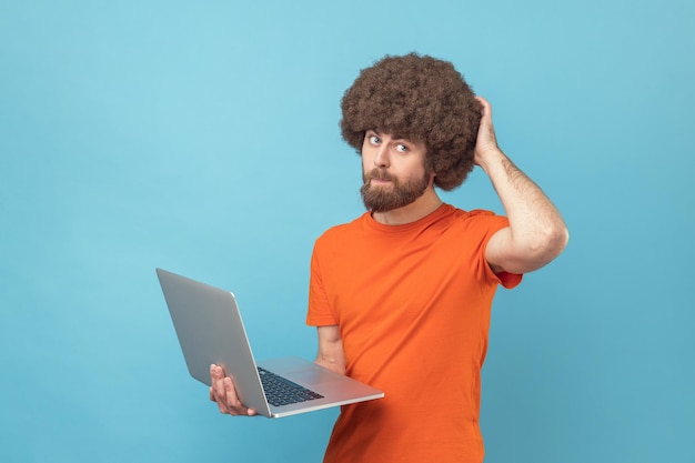 Homme tenant un ordinateur portable et pensant à un nouveau projet se grattant l'arrière de la tête