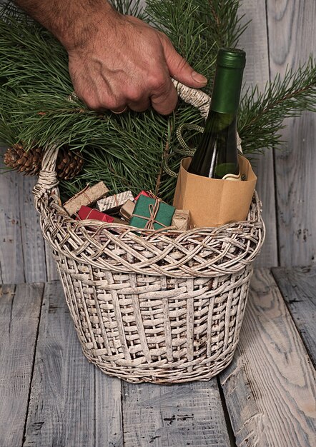 Homme tenant un panier avec des cadeaux de Noël, des branches de pin et une bouteille de vin