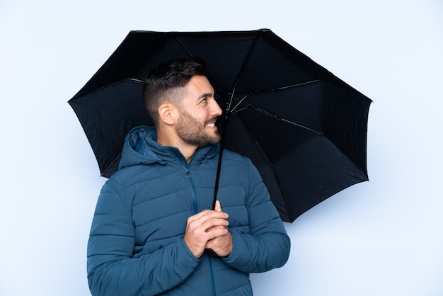 Homme tenant un parapluie sur un mur isolé avec une expression heureuse