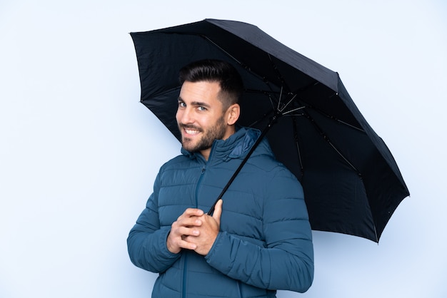 Homme tenant un parapluie sur un mur isolé, souriant beaucoup