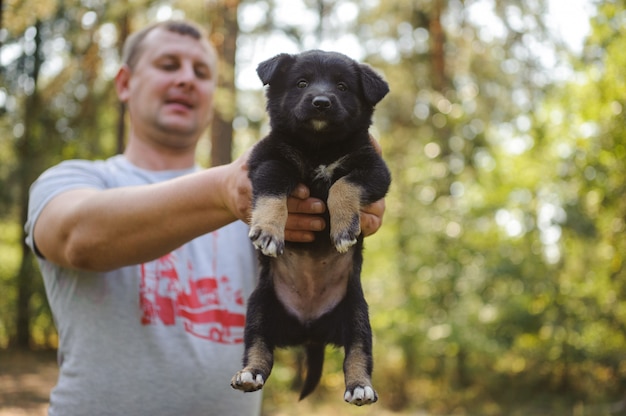 Photo homme tenant un petit chiot noir en regardant la caméra dans la forêt