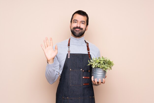 Homme tenant une plante sur fond isolé, saluant avec la main avec une expression heureuse